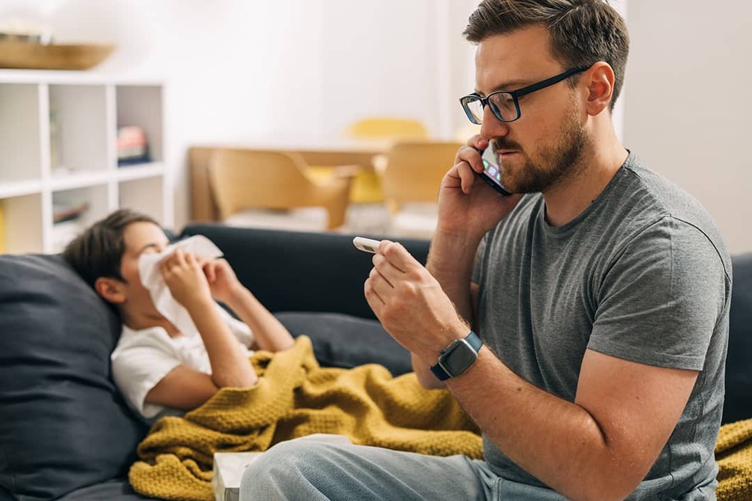 A parent calling a pediatrician over the phone, while checking his child's body temperature due to the flu.